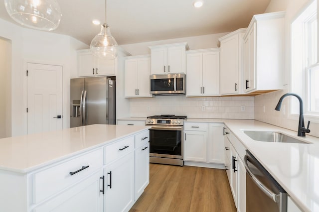 kitchen with decorative backsplash, a kitchen island, stainless steel appliances, light wood-type flooring, and a sink