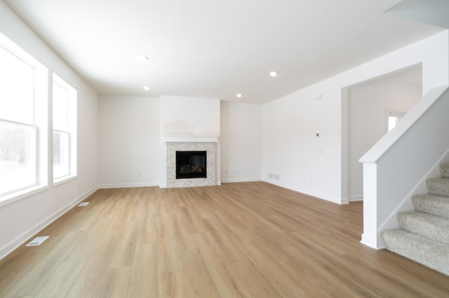 unfurnished living room with light wood finished floors, visible vents, a glass covered fireplace, stairway, and recessed lighting