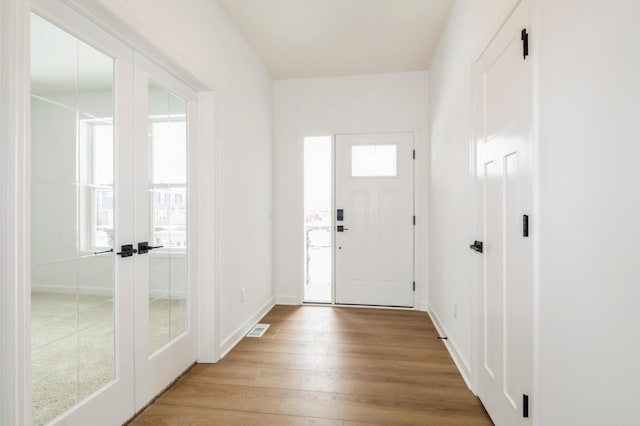 entryway with light wood-type flooring, french doors, visible vents, and baseboards