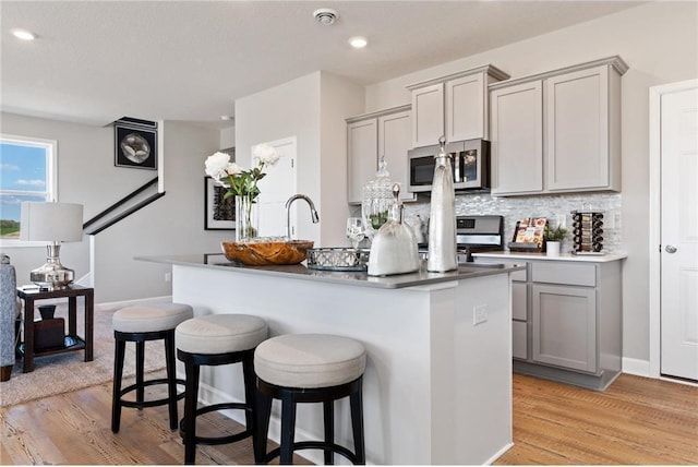 kitchen with stainless steel appliances, light wood-type flooring, gray cabinets, and a kitchen island with sink