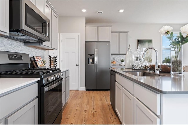 kitchen with light wood-style flooring, recessed lighting, stainless steel appliances, a sink, and decorative backsplash