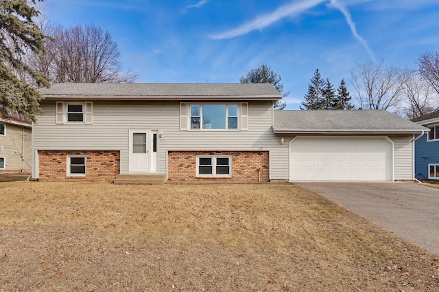 split foyer home with driveway, an attached garage, a front yard, and brick siding