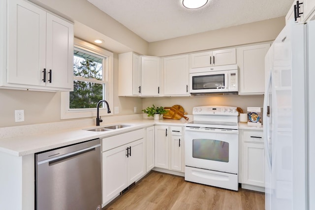 kitchen with light wood-style flooring, white appliances, a sink, white cabinets, and light countertops