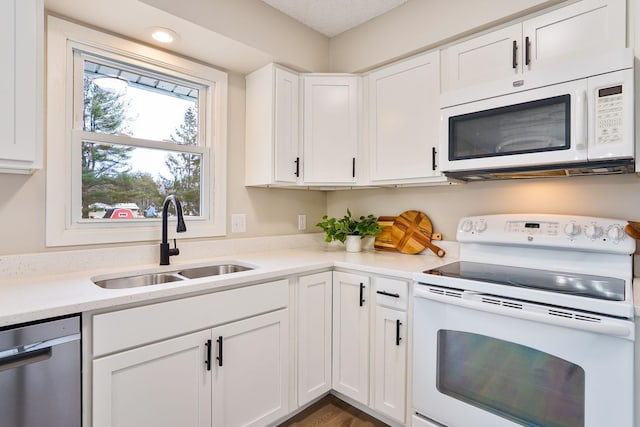 kitchen with white appliances, white cabinets, a sink, and light countertops