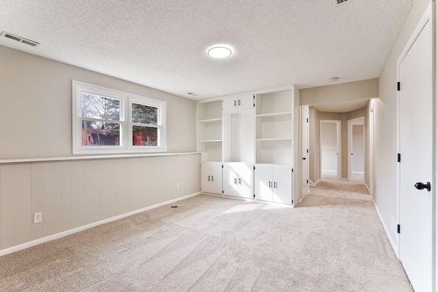 unfurnished bedroom with light carpet, a textured ceiling, wainscoting, and visible vents