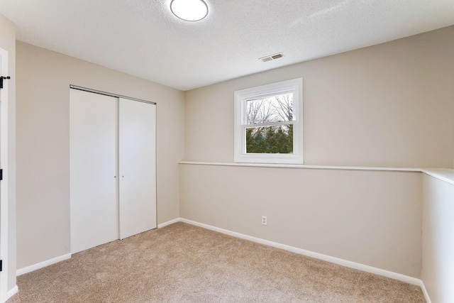 unfurnished bedroom with baseboards, visible vents, a textured ceiling, carpet flooring, and a closet