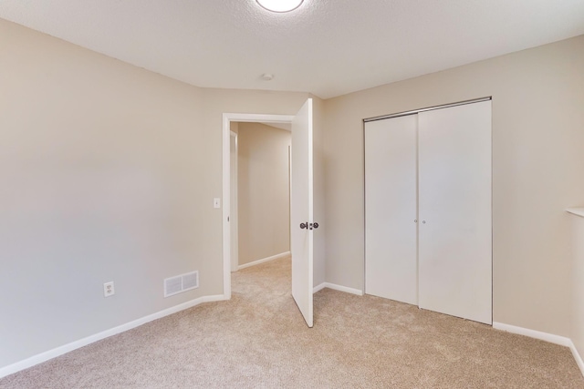 unfurnished bedroom with light carpet, baseboards, visible vents, and a closet