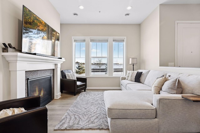 living room featuring light wood finished floors, recessed lighting, baseboards, and a glass covered fireplace