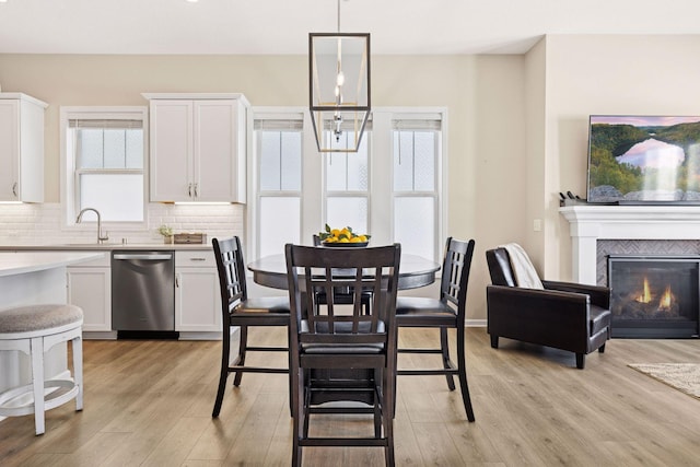 dining space featuring light wood finished floors, baseboards, a chandelier, and a glass covered fireplace