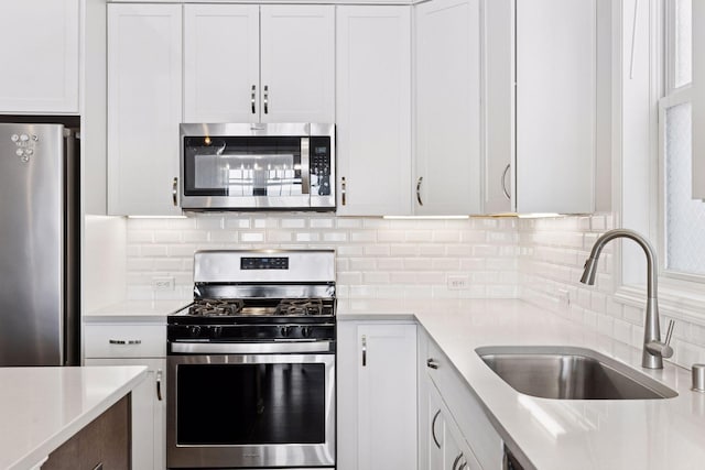 kitchen with white cabinets, decorative backsplash, appliances with stainless steel finishes, light countertops, and a sink