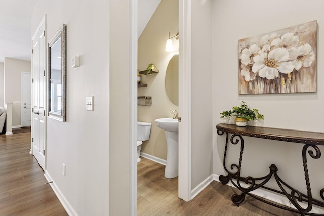 hallway featuring a sink, baseboards, and wood finished floors