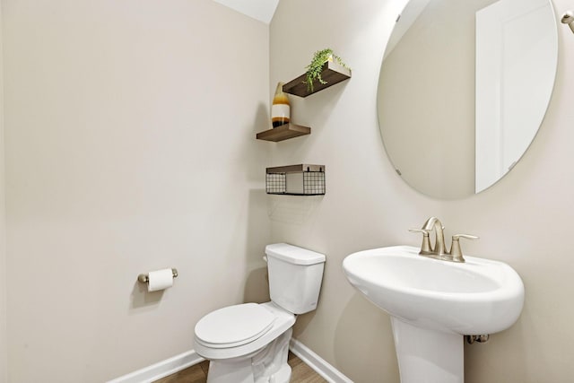 half bathroom featuring a sink, wood finished floors, toilet, and baseboards