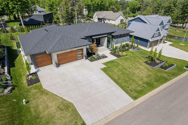 view of front of property featuring roof with shingles, concrete driveway, a front yard, a garage, and a residential view