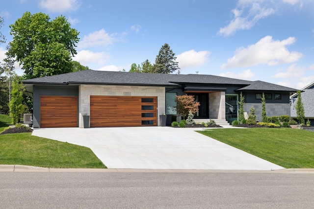 view of front facade with a garage, driveway, a shingled roof, stone siding, and a front lawn