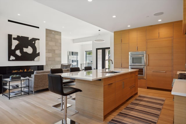 kitchen featuring light wood finished floors, light countertops, open floor plan, a sink, and a warm lit fireplace