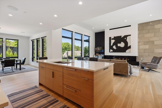 kitchen with light wood-style floors, a glass covered fireplace, open floor plan, an island with sink, and modern cabinets