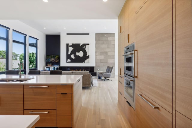 kitchen featuring light countertops, light wood-style floors, a sink, modern cabinets, and a warm lit fireplace