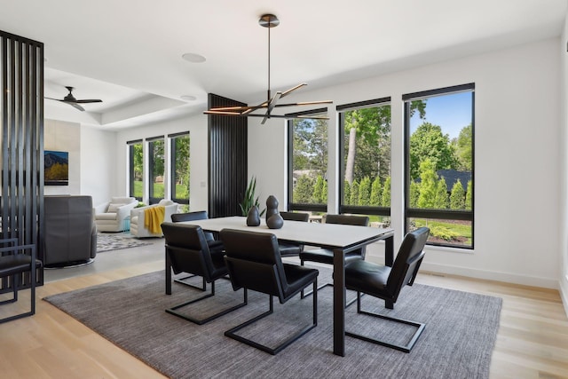 dining room with light wood-style floors, a tray ceiling, baseboards, and ceiling fan with notable chandelier