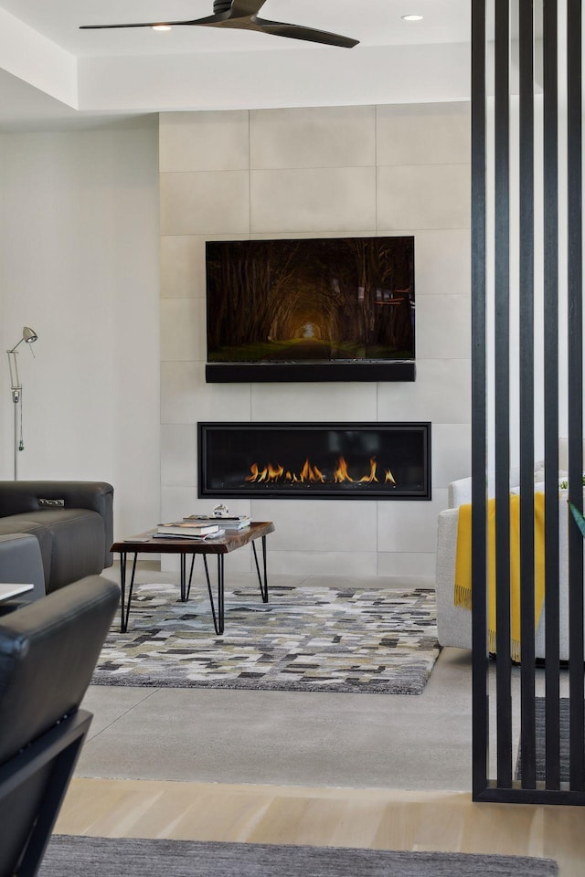 living area with a ceiling fan, a tile fireplace, and wood finished floors