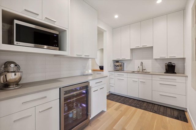 kitchen with wine cooler, light countertops, stainless steel microwave, light wood-style floors, and a sink