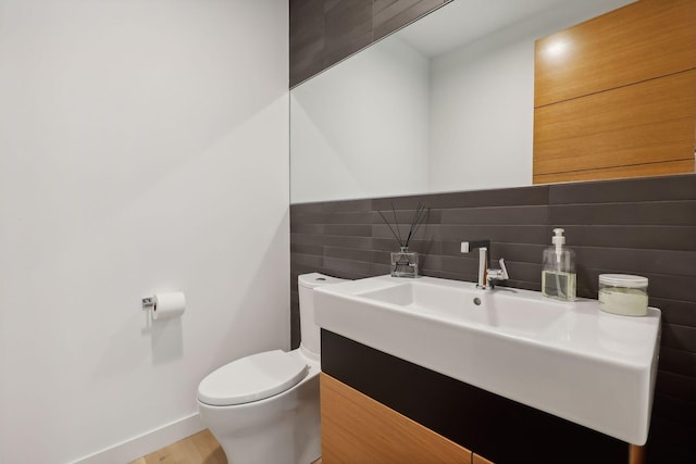 half bathroom featuring toilet, baseboards, and vanity