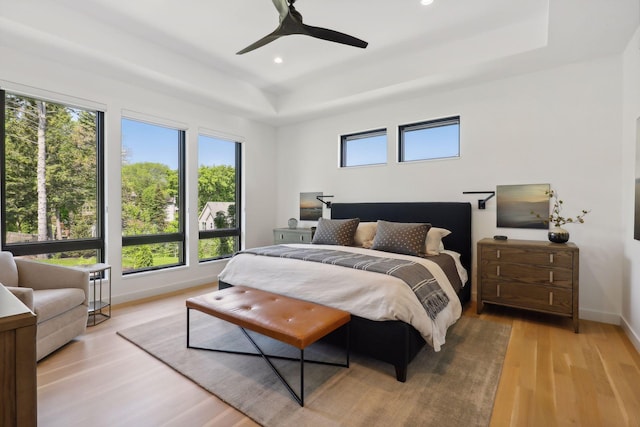 bedroom featuring baseboards, a raised ceiling, a ceiling fan, light wood-style floors, and recessed lighting