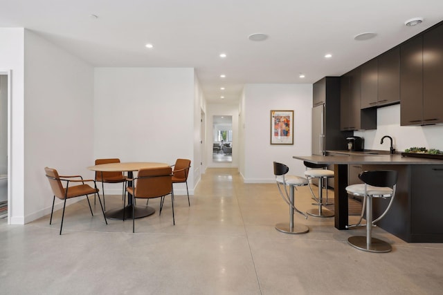 kitchen with dark countertops, a kitchen breakfast bar, concrete flooring, a sink, and recessed lighting