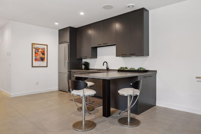 kitchen with finished concrete floors, baseboards, a sink, and a breakfast bar area