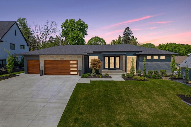 view of front of property featuring an attached garage, a shingled roof, driveway, stone siding, and a lawn