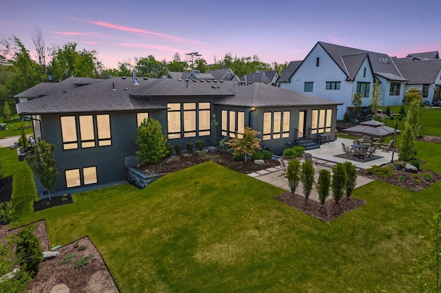 rear view of house with a patio area, a yard, and roof with shingles