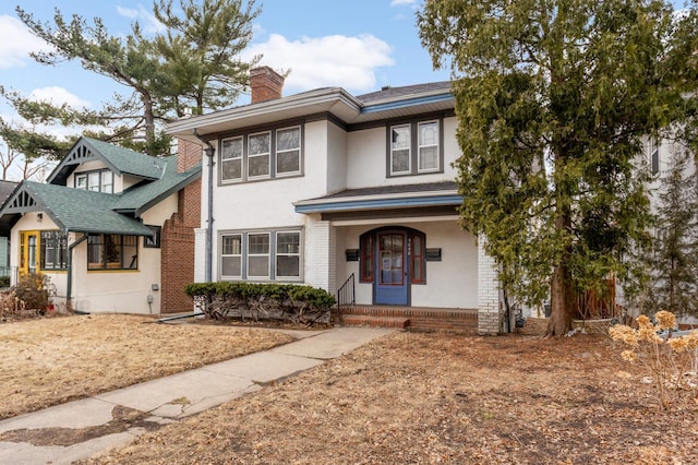 view of front of property featuring brick siding, a chimney, covered porch, and stucco siding