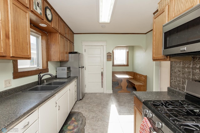 kitchen featuring a sink, dark countertops, arched walkways, appliances with stainless steel finishes, and crown molding