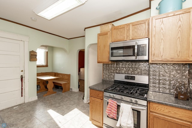 kitchen featuring dark countertops, arched walkways, appliances with stainless steel finishes, crown molding, and decorative backsplash