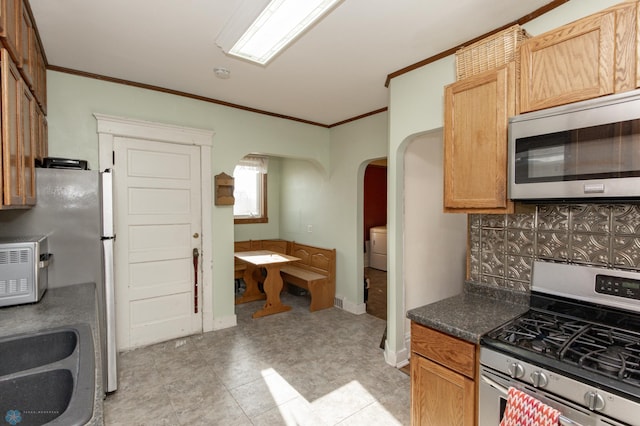 kitchen with arched walkways, ornamental molding, decorative backsplash, appliances with stainless steel finishes, and dark countertops