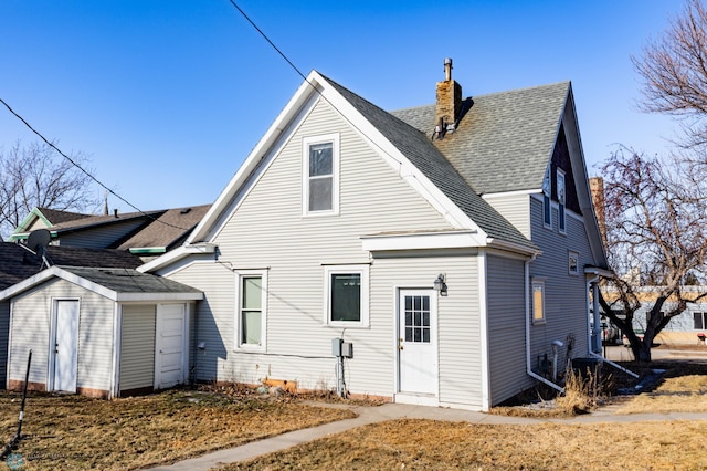 rear view of house with a storage shed, an outdoor structure, roof with shingles, and a chimney