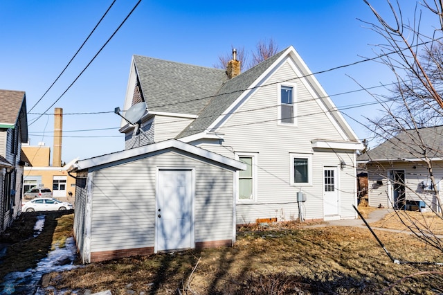 back of property with a chimney, a shingled roof, and an outdoor structure