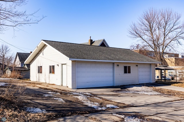 view of side of home featuring a detached garage, roof with shingles, and a chimney