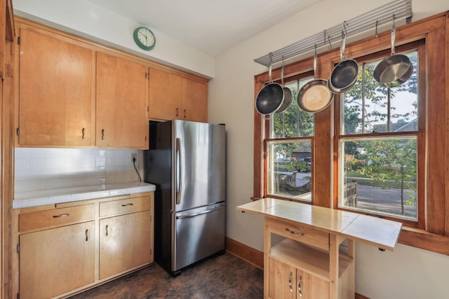 kitchen with baseboards, tile counters, backsplash, and freestanding refrigerator