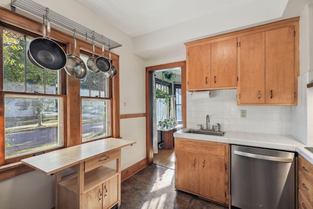 kitchen featuring tile countertops, a sink, stainless steel dishwasher, tasteful backsplash, and plenty of natural light