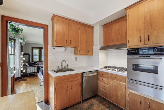 kitchen with under cabinet range hood, stainless steel appliances, a sink, decorative backsplash, and a warming drawer