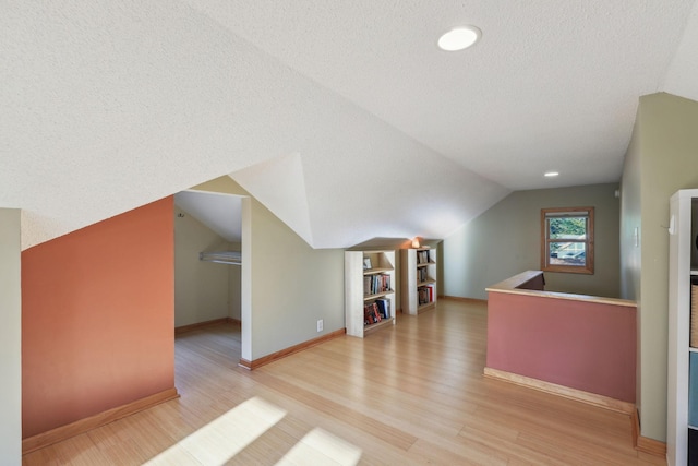 bonus room with a textured ceiling, vaulted ceiling, wood finished floors, and baseboards