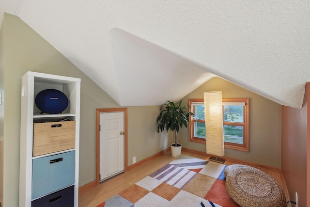 bonus room with lofted ceiling, light wood-style floors, baseboards, and a textured ceiling