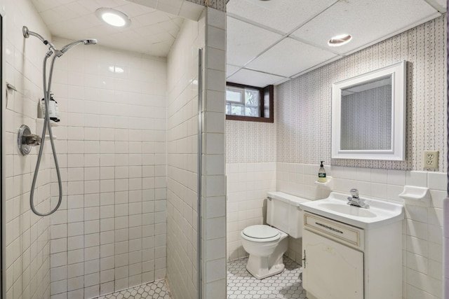 bathroom featuring toilet, wallpapered walls, a wainscoted wall, and a stall shower