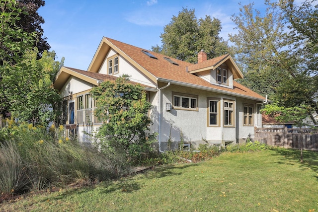 view of property exterior with a chimney, stucco siding, a shingled roof, a lawn, and fence