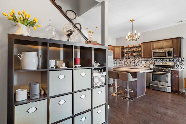 kitchen featuring light countertops, a kitchen bar, decorative backsplash, appliances with stainless steel finishes, and dark wood-style floors