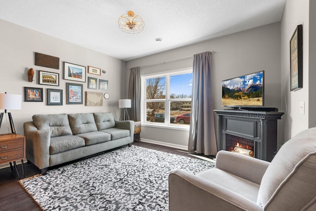 living area with a warm lit fireplace, a textured ceiling, baseboards, and wood finished floors