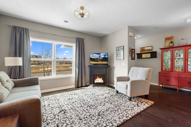 living room featuring baseboards, a textured ceiling, a warm lit fireplace, and wood finished floors