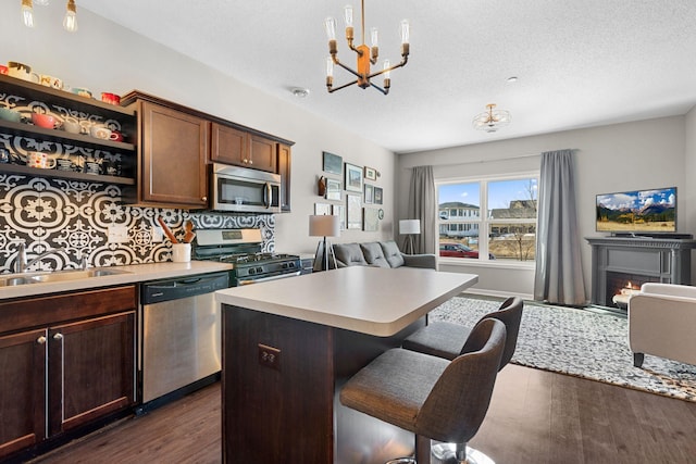 kitchen featuring open floor plan, light countertops, a lit fireplace, stainless steel appliances, and dark wood-style flooring