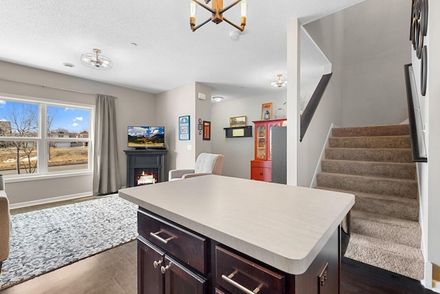 kitchen featuring a kitchen island, a warm lit fireplace, light countertops, a textured ceiling, and open floor plan