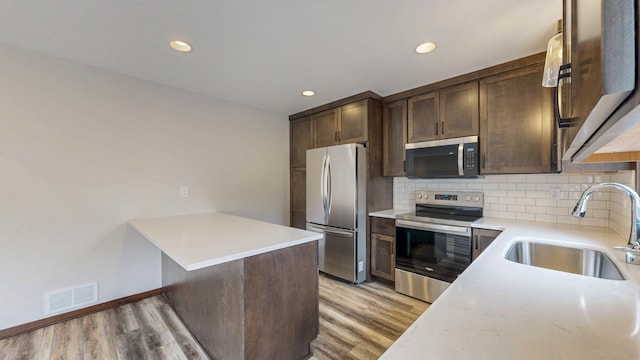 kitchen featuring stainless steel appliances, a sink, visible vents, dark brown cabinets, and decorative backsplash